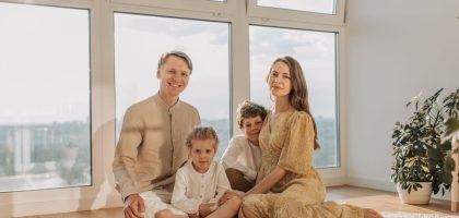 A cheerful family of four sitting together on the floor of a sunlit living room.