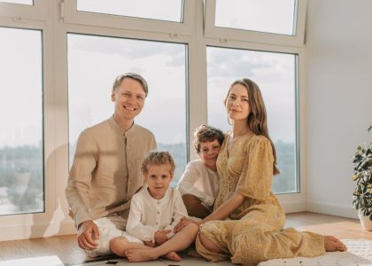 A cheerful family of four sitting together on the floor of a sunlit living room.